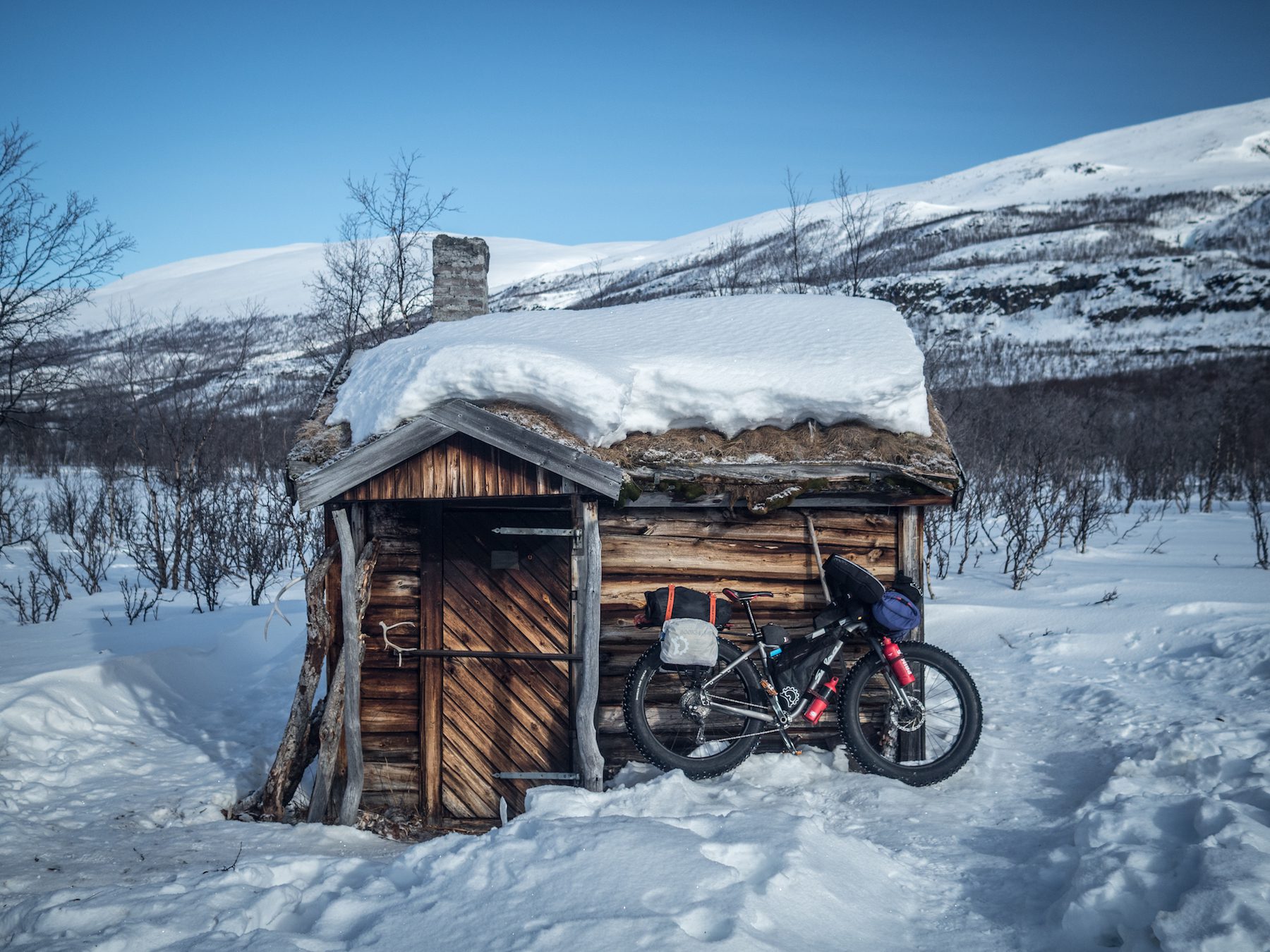 "This tiny cabin was nestling in the upper reaches of a heavily wooded valley; we spotted it as we wound our way up the snowmobile trail along the frozen river on a sunny morning, at the beginning of our homeward journey. The interior contained a fully-equipped living space, only in miniature. The mandatory cast-iron stove, a sink, bed and sitting space. Axe, saw and fishing gear, all neatly arranged and left clean and tidy by the few visitors who had spent the night there. It reminded us instantly of the Scottish bothies that dot our home hills, only these caretakers seemed to respect it more. Although silent and cold, it radiated the lived-in warmth of a place that has seen many hands, many memories, and many nights spent in comfort. If only we had gone a few more kilometres the night before, we might have been able to add our own. Next time!" ~Huw Oliver