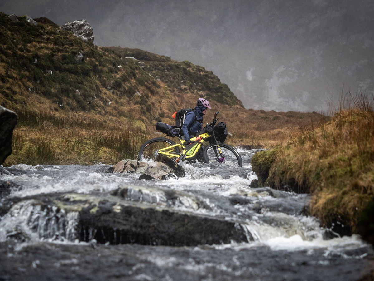 Annie carries her bike across a river